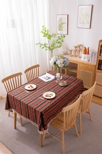 Close-up of bohemian striped tablecloth with thick white tassels on a wooden dining table