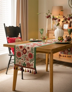 Close-up of vintage floral table runner with colorful tassels on a wooden dining table