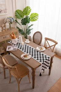 Detail of checkered table runner with black tassels on dark wood dining table