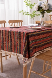 Detail of bohemian striped tablecloth with white tassels on a rustic wooden dining table