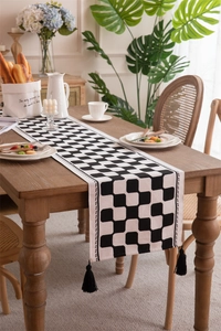 Close-up of black and white checkered table runner with thick tassels on wooden table