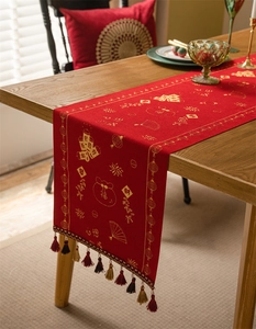 Macro detail of red festive table runner with golden patterns and colorful tassel trim