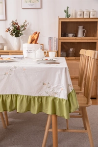 Detail of floral embroidery and green ruffle edge on a cream cotton tablecloth