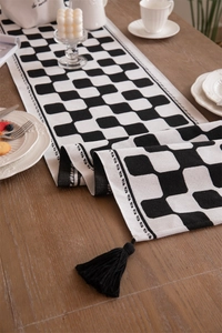 Macro shot of black and white checkered table runner with thick fringe on a wood surface