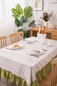 Detail of floral embroidery and green ruffled edge on beige cotton tablecloth