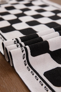 Close-up of checkered jacquard table runner with black geometric fringe on wood surface