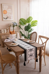 Close-up of black and white geometric table runner with tassels on a dark wood table