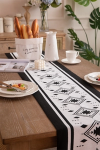 Close-up of black and white geometric table runner with tassels on a wooden dining table
