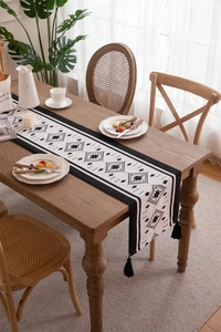 Detailed view of checkered table runner with black tassels on rustic wooden dining table