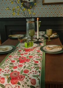 Dettaglio del runner da tavolo con rose rosse e foglie verdi su tessuto beige