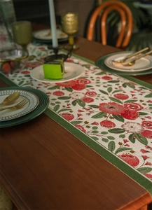 Dettaglio del runner da tavola jacquard a fiori rossi con bordo verde su tavolo in legno