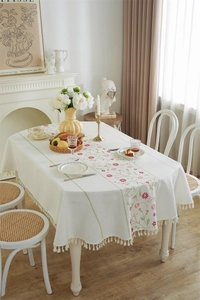 Detailed close-up of floral embroidery and white cotton tassel fringe on a rectangular tablecloth