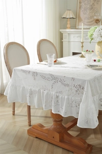 Détail d'une nappe en dentelle crème avec motifs jacquard floraux et bordures à volants