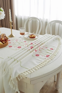 Detail of red floral embroidery and beige tassels on cream textured festive tablecloth