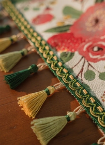 Dettaglio del runner da tavolo in jacquard con motivi di rose rosse e nappe di seta