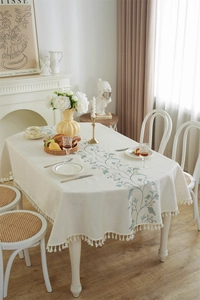 Close-up of floral embroidery and cotton tassels on a beige linen tablecloth