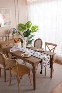 Detail of black and white floral table runner with tassels on a rustic wood surface