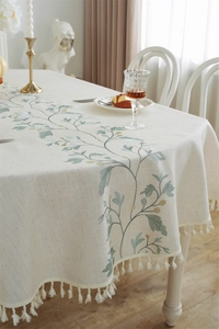 Close-up of olive leaf embroidery and cream fringe details on a linen texture tablecloth