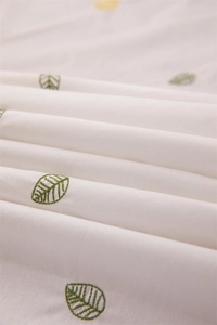 Macro shot of green leaf embroidery on white cotton fabric with soft ruffles and elegant folds