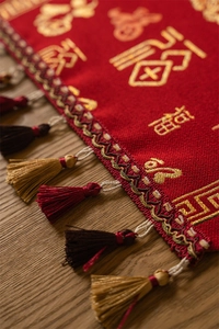 Detailed close-up of Chinese New Year table runner with gold Fu character embroidery and tassels
