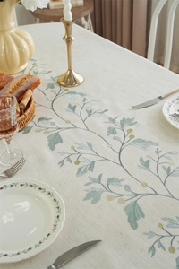 Detailed embroidery of green plant leaves on a heavy cream linen tablecloth for dining