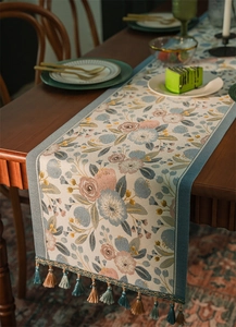 Dettaglio runner da tavola jacquard floreale con nappe su un tavolo di legno