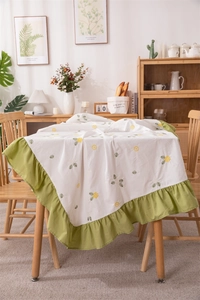 Detail of white cotton tablecloth featuring yellow floral embroidery and green ruffled edges