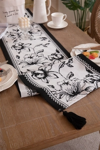 Detail of floral jacquard table runner with black tassels on rustic wooden table
