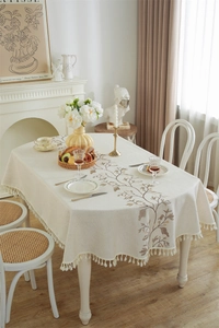 Close-up of cream rectangular tablecloth featuring brown floral embroidery and white tassels