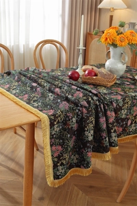 Detail of vintage floral jacquard tablecloth featuring golden fringe tassels on table