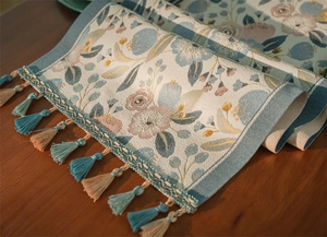 Dettaglio del runner da tavolo jacquard con motivi floreali blu ed eleganti nappe a frangia