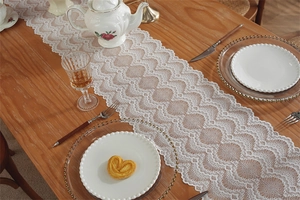 Makro-Detail des französischen weißen Spitzen-Tischläufers mit Wellenrand auf Holztisch