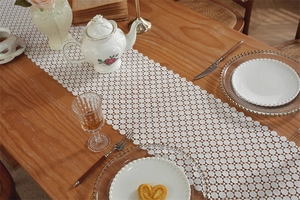 Detailed view of white hollow lace table runner with floral patterns on wooden table