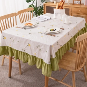 Floral embroidered cotton tablecloth with green ruffle edges in a cozy dining room
