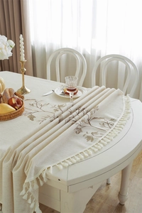 Detailed embroidery of brown floral patterns on beige linen tablecloth with white tassels