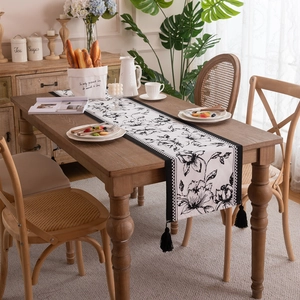 Modern black and white floral table runner with tassels on a dark wood dining table
