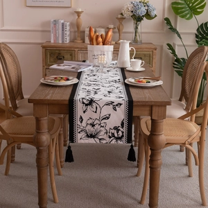 Black and white floral jacquard table runner with fringe tassels on a wooden dining table