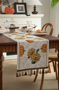 Detail of autumn table runner with orange pumpkins and tassels on a wooden dining table