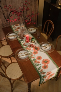 Dettaglio runner da tavola con margherite arancioni, bordo verde scuro e nappe eleganti