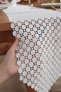 Detail of white lace table runner with hollow polka dot patterns on wooden table