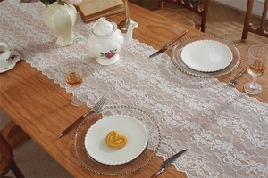 Detailansicht weißer Spitzen-Tischläufer mit floralem Muster und Wellenrand