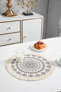 Détail d'un set de table rond à motif mandala avec franges en coton sur une table blanche