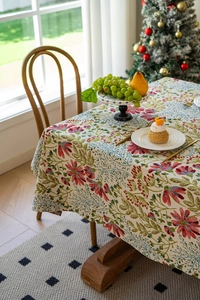 Detail einer Vintage-Tischdecke mit roten Blumen, grünen Pflanzen und Fransenrand
