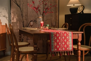 Dettaglio del runner da tavola jacquard rosso con motivi floreali e nappe bicolori su legno