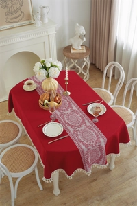 Close-up of red festive tablecloth with white lace pattern and decorative tassel fringe