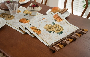 Detail of autumn table runner with pumpkin and sunflower patterns and decorative tassels