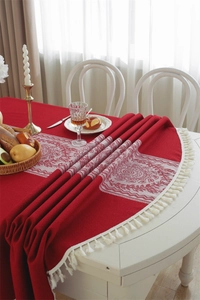 Detailed texture of red jacquard tablecloth with white tassel edge on a wooden table