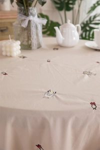 Detail of embroidered owl patterns on beige cotton tablecloth with ruffled edges
