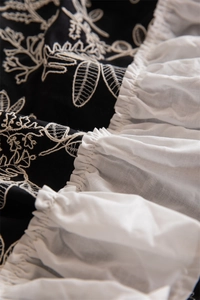 Detail of floral embroidery on black cotton fabric with white ruffled edges and textures