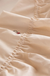 Detailed macro view of beige cotton tablecloth featuring elegant layered ruffles and red floral embroidery